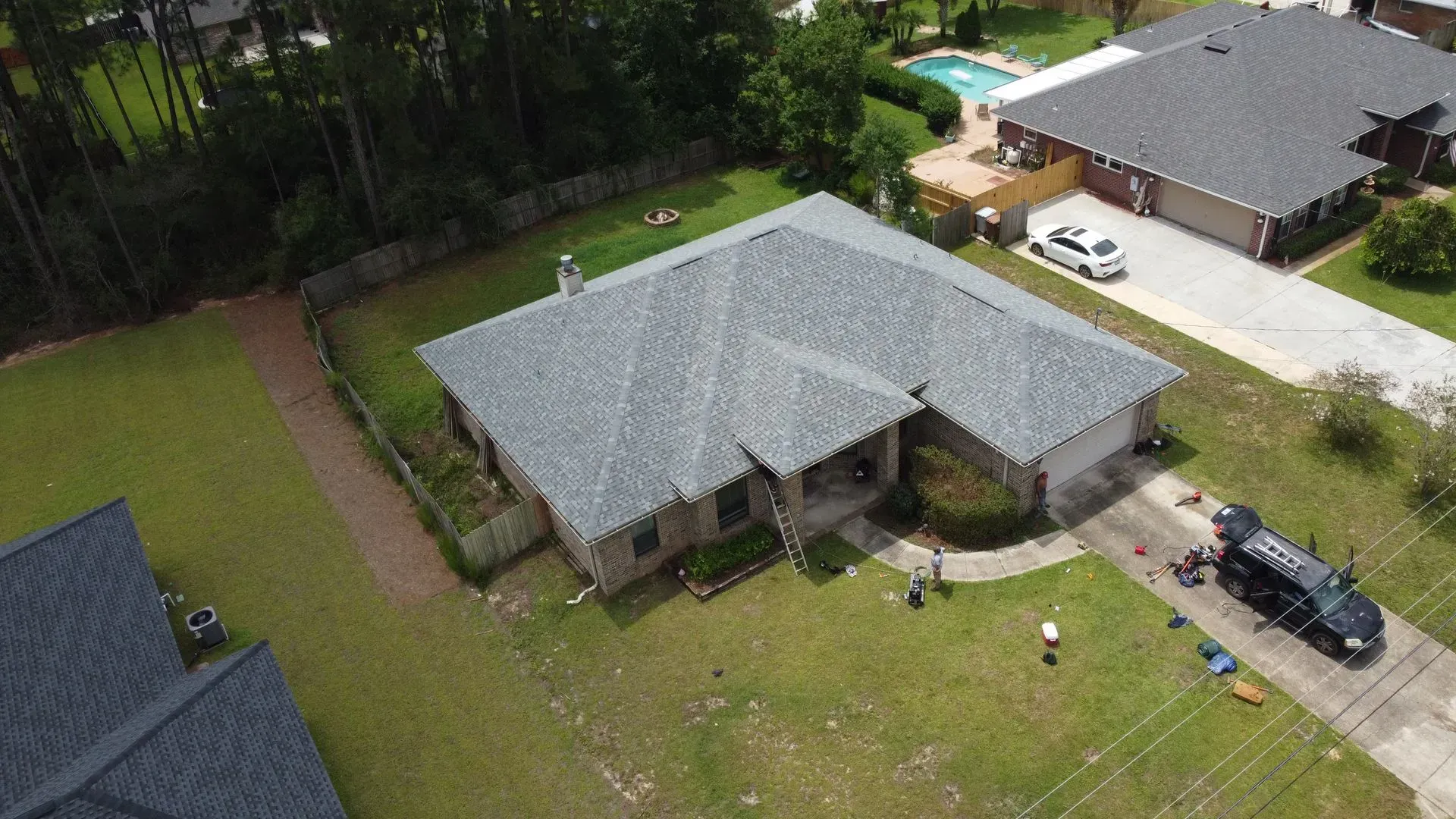 Aerial view of a gray-roofed house with a circular driveway and yard. A black van is parked nearby.
