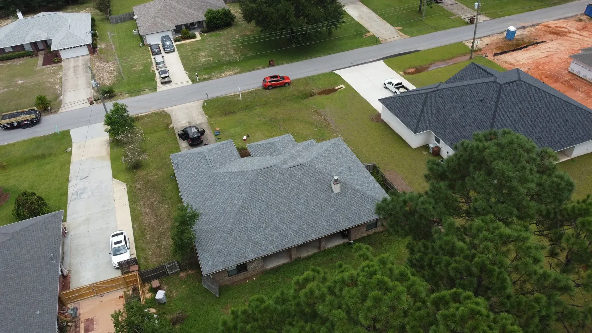 Aerial view of houses with gray rooftops and driveways, surrounded by green lawns and a street.