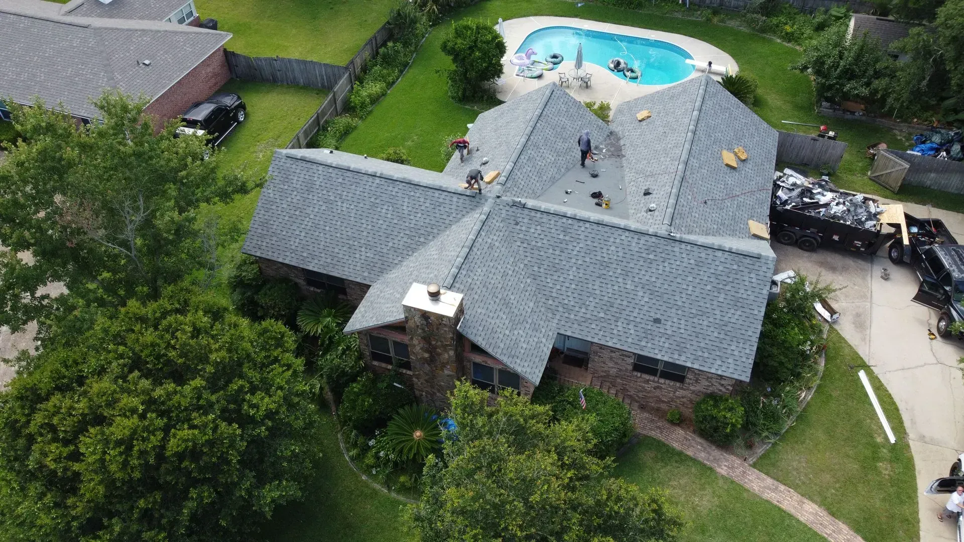 Aerial view of a house with roofers working on the roof; pool in the backyard.