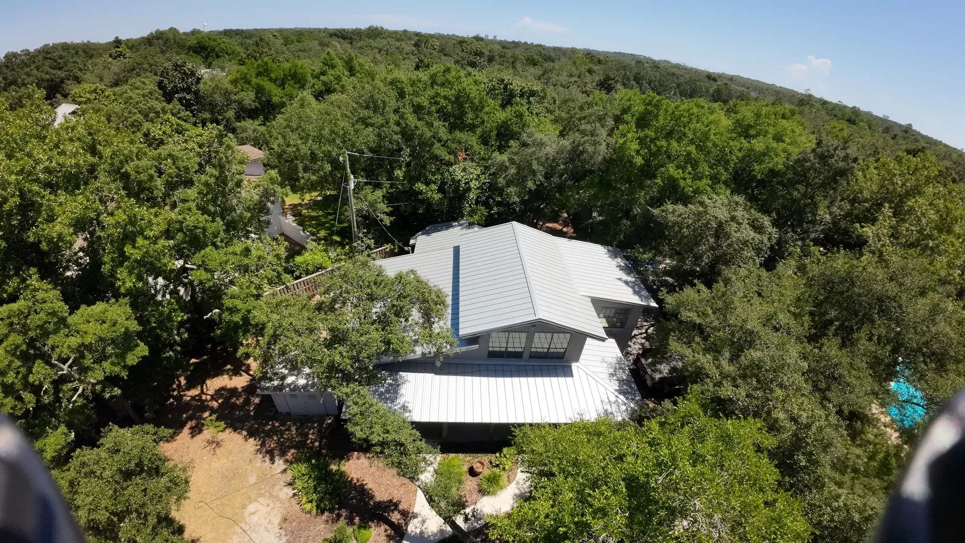 House nestled in a forest of green trees, white roof.