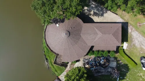 Overhead view of a circular building with a brown roof next to a body of water and green trees.