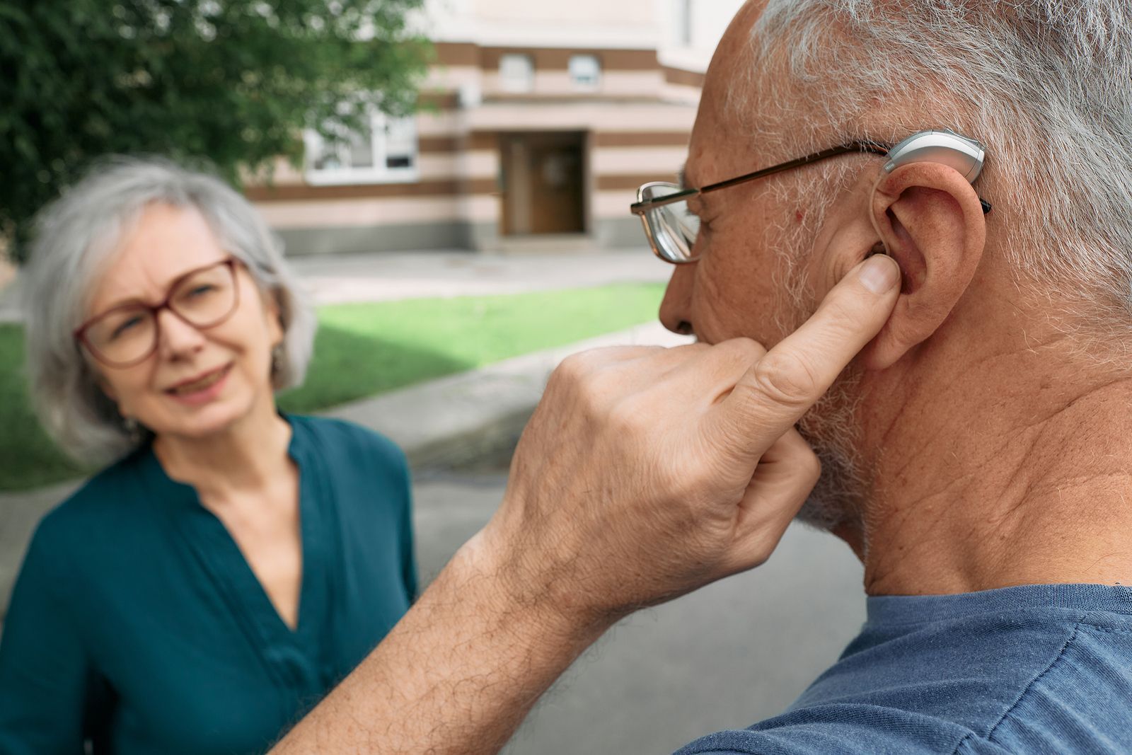 A man is putting a hearing aid in his ear while a woman looks on.