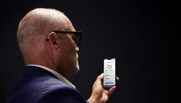 A man wearing a hearing aid is holding a cell phone.