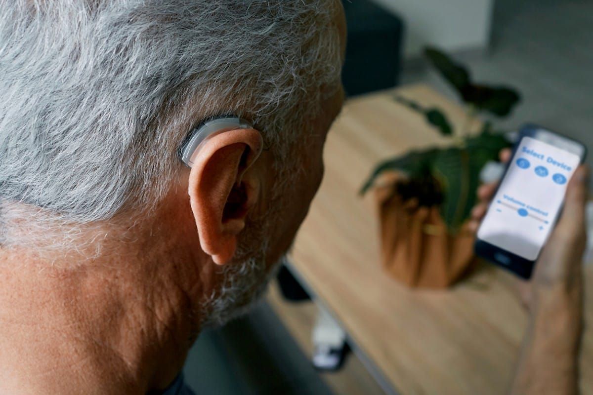 A man wearing a hearing aid is using a smart phone.