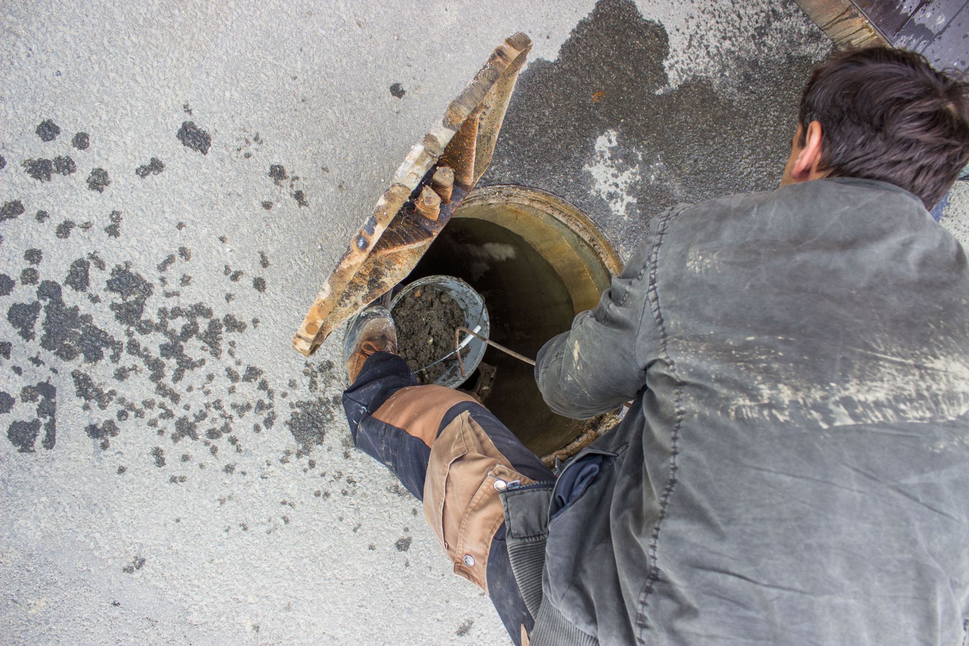 Man working on a manhole in the street. He is opening the cover and looking inside.