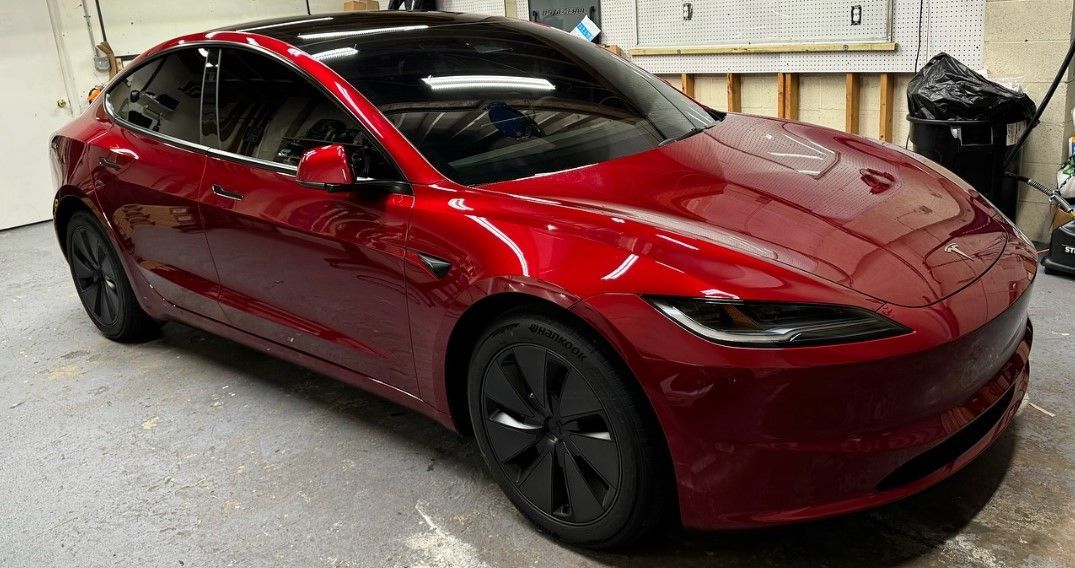 A red tesla model 3 is parked in a garage.