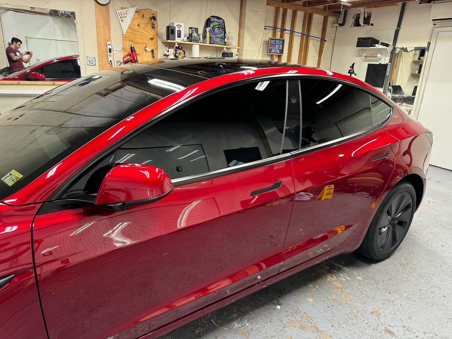 A red tesla model 3 is parked in a garage.