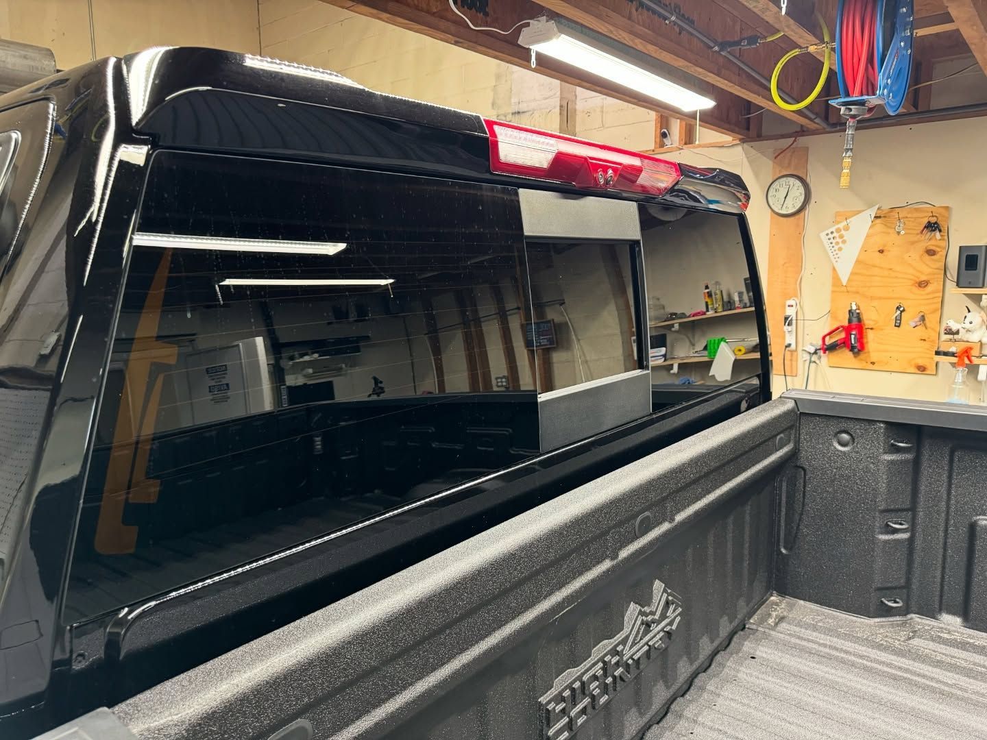 A black truck with a red tail light is parked in a garage.