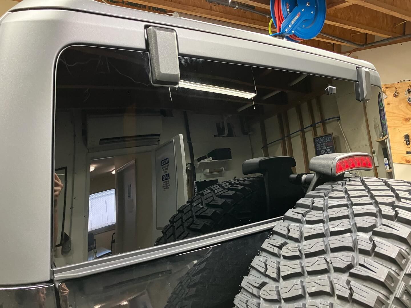 A jeep is parked in a garage with a tire on the back of it.