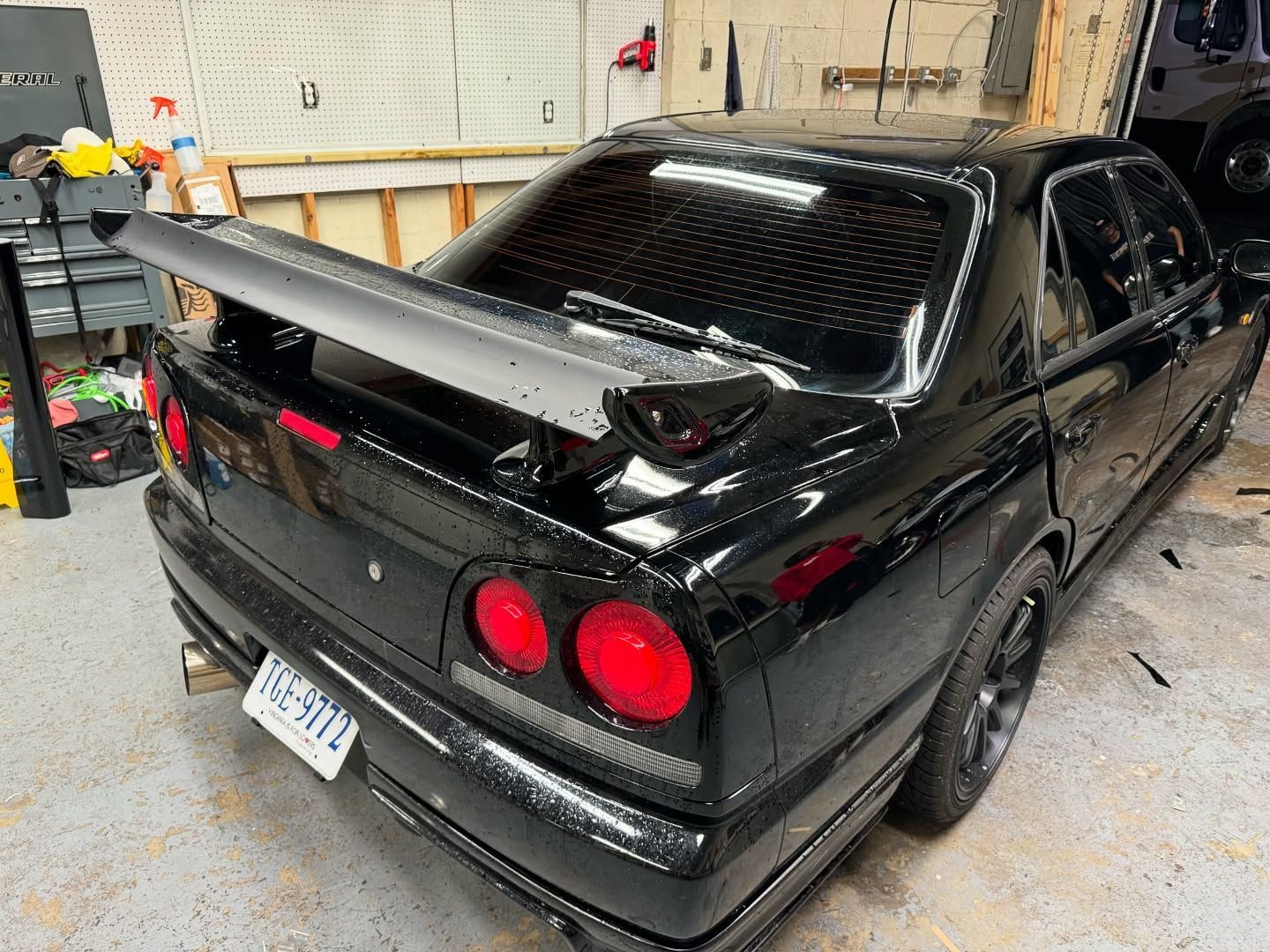 A black car with a spoiler on the back is parked in a garage.