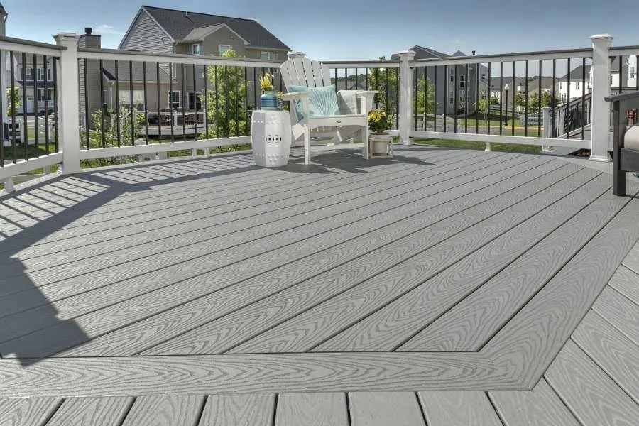 Gray composite deck with white railing, chair, and water cooler, in a backyard.