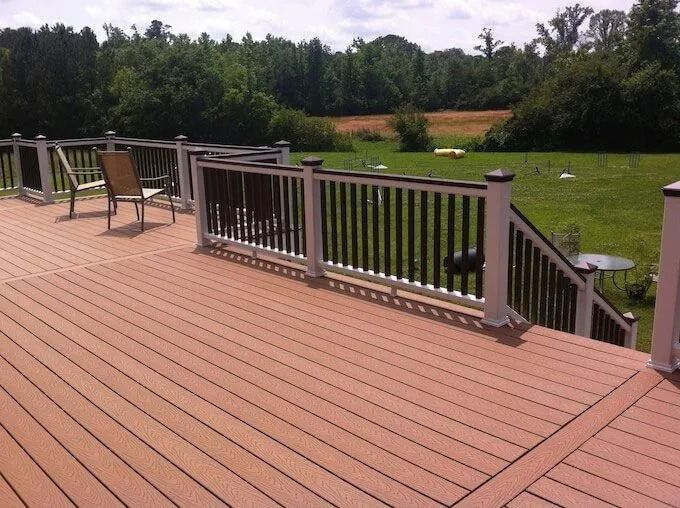 A spacious brown composite deck with white and dark railings, overlooking a green lawn and trees.