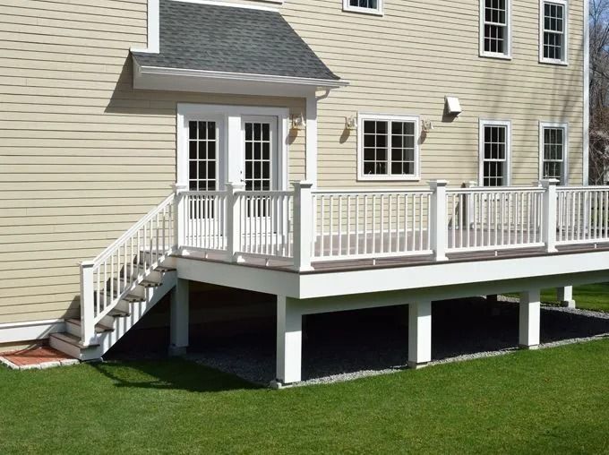 Beige house with white deck, stairs, and railings, overlooking green grass.