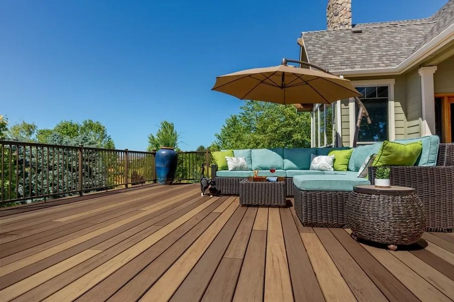 A sunny deck with brown composite wood, teal outdoor sofa, umbrella, and blue sky.