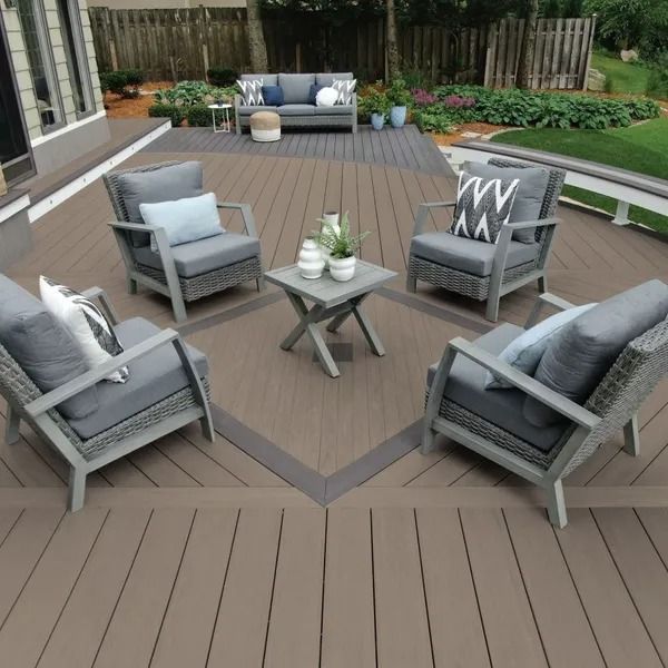Outdoor deck with gray furniture arranged around a small table, plants, and a backyard.