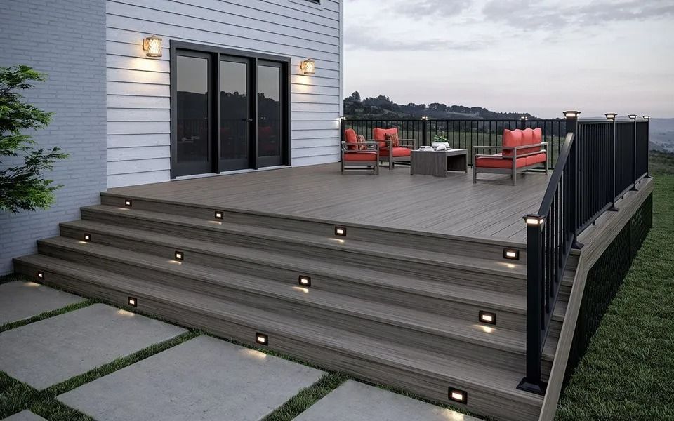 Deck with steps, built-in lights, black railing, and outdoor furniture. Lawn and house in background.