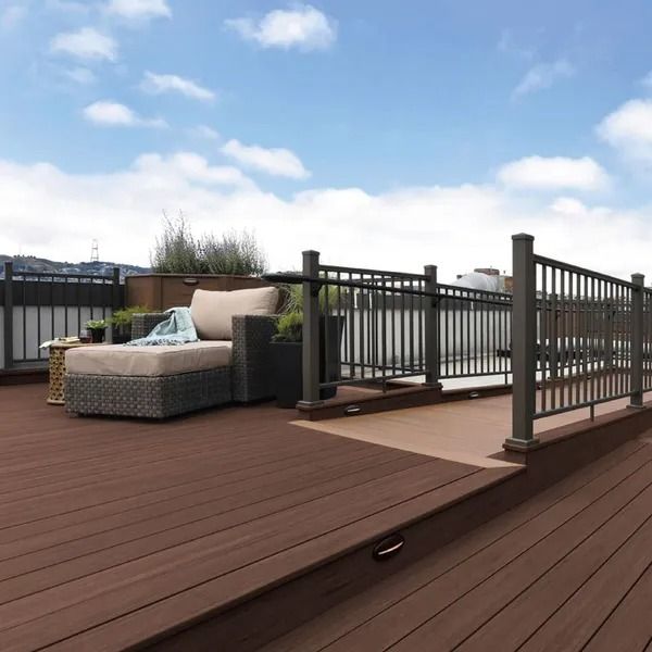 Rooftop deck with brown composite boards, dark railing, and outdoor seating. Sky with clouds in the background.