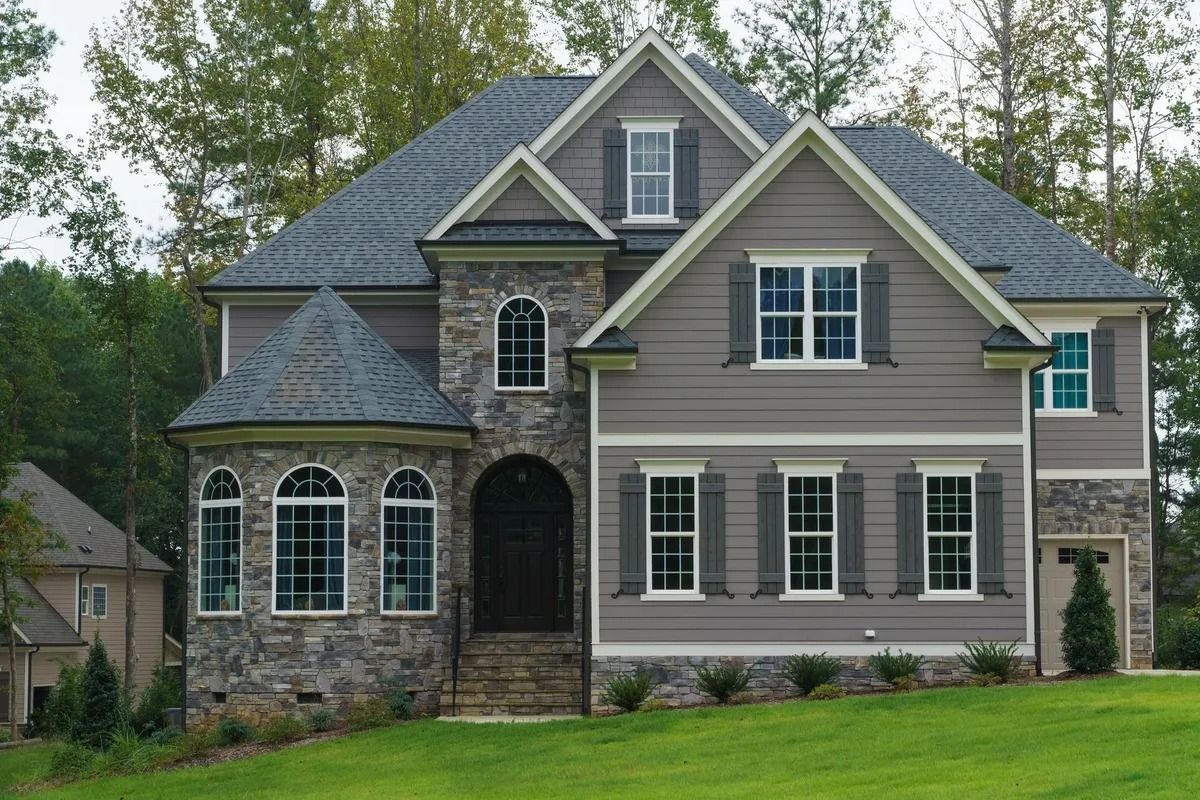 Gray and stone-faced two-story house with gray shutters, set on a grassy lawn.