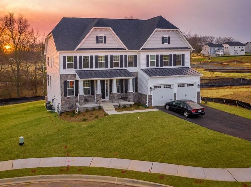 Two-story white house with black shutters, stone accents, and a two-car garage; car parked in the driveway, dusk.