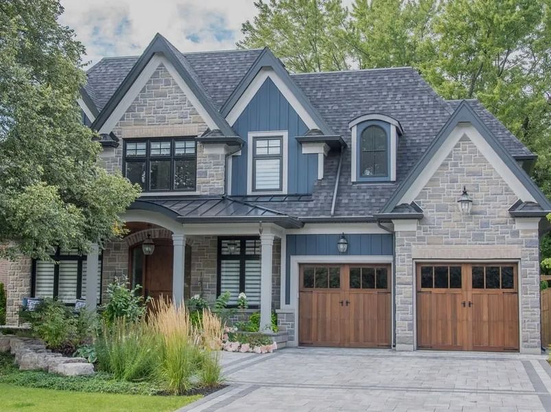 Two-story house with blue siding, stone facade, brown garage doors, and a gray roof.