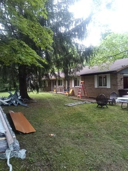 Backyard with a brick house, green lawn, trees, and construction materials.