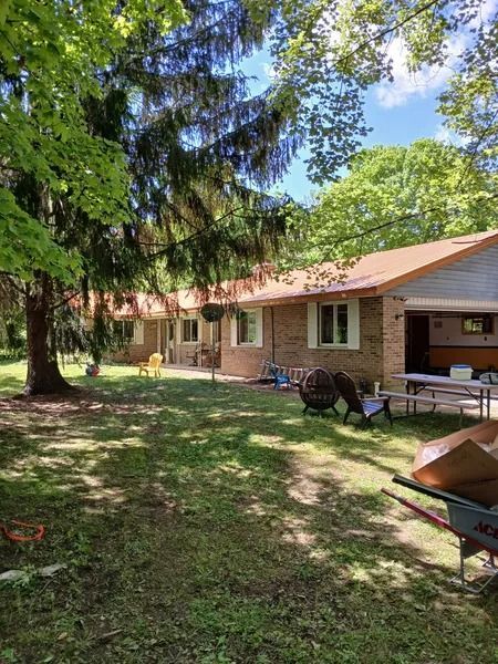 A one-story brick building with a brown roof, trees, and a grassy yard.