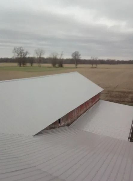 Barn with red siding and a gray metal roof, set in a field on an overcast day.