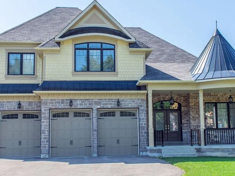 A two-story house with a stone facade, three-car garage, and a covered entrance under a blue sky.
