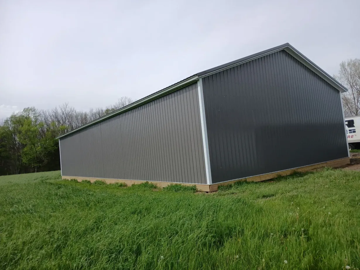 Gray metal barn on a grassy field, trees in the background, overcast sky.