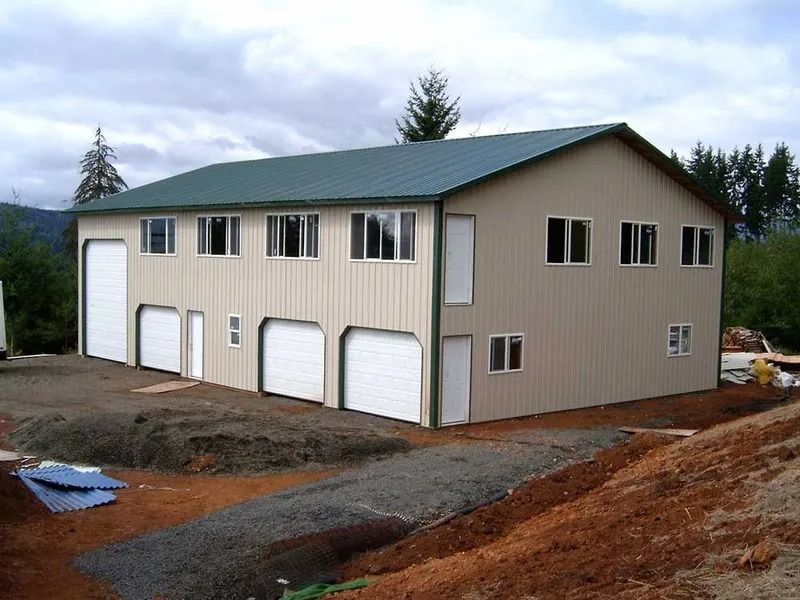 Two-story beige metal building with a green roof and multiple garage doors. Set on a dirt lot.