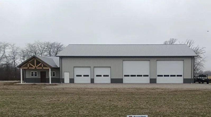 Grey metal building with garage doors and porch; exterior view.