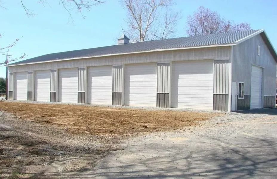 Gray metal building with multiple garage doors, on a gravel lot, under a blue sky.