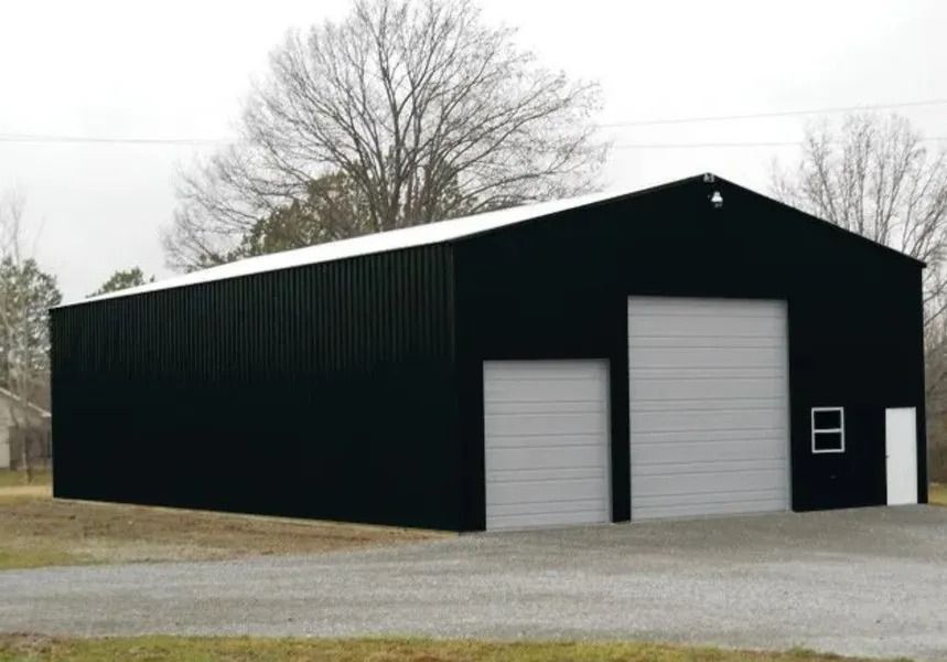 Black metal industrial building with white doors and roof, gravel driveway.