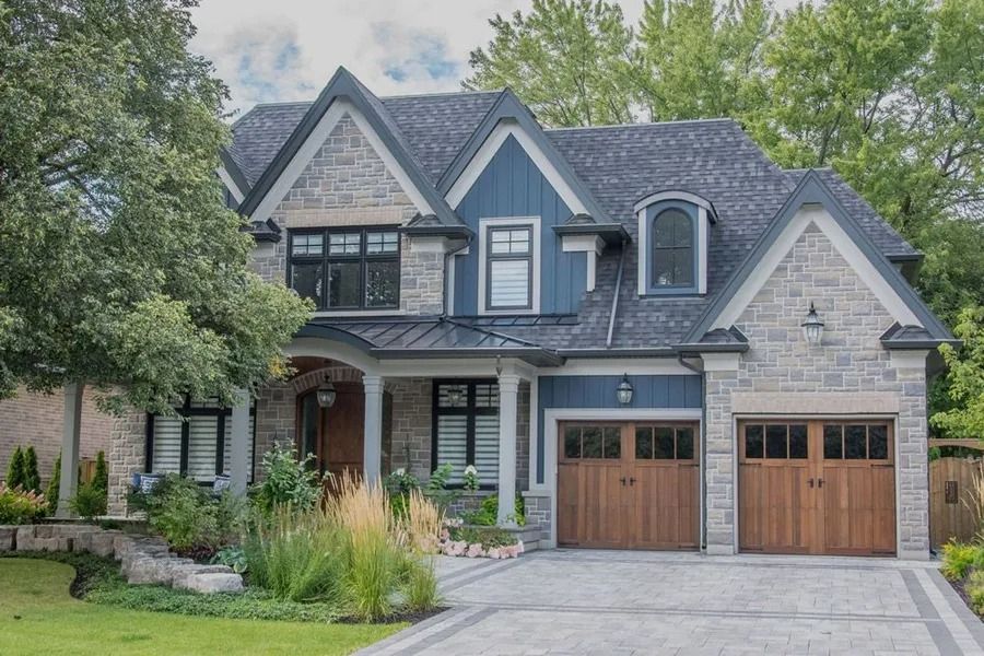 Two-story house with blue siding, stone accents, and wooden garage doors, set on a manicured lawn.