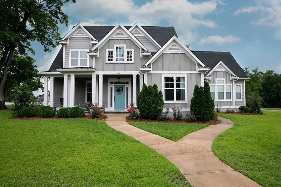 Gray two-story house with white trim, blue door, and a brick pathway on a green lawn.
