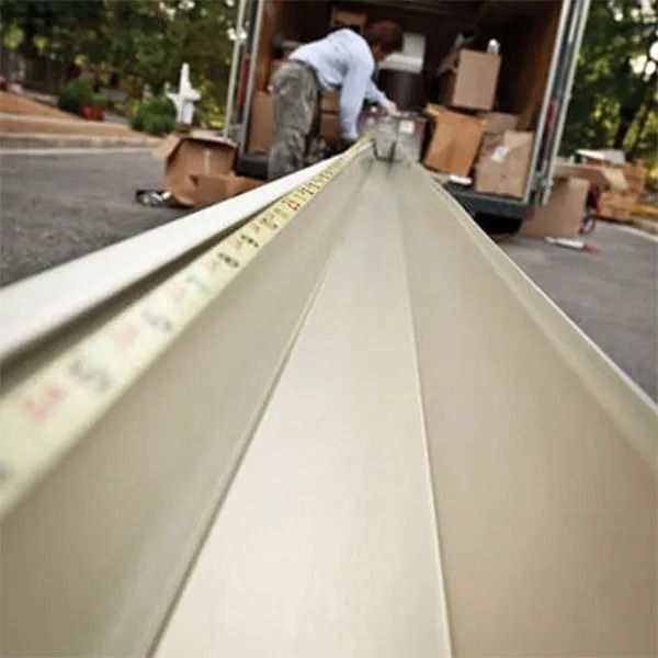 Man measures gutter, boxes in truck, on residential street.