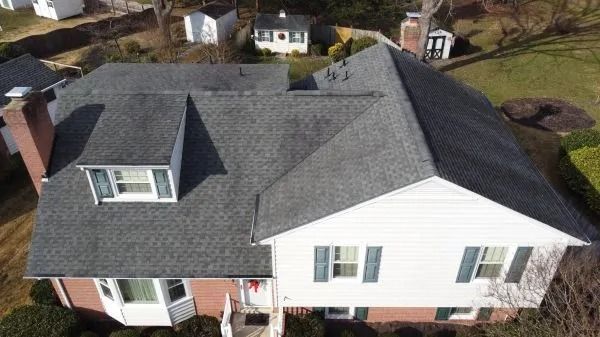 Overhead view of a house with a gray shingle roof, red brick, and white siding, surrounded by trees.