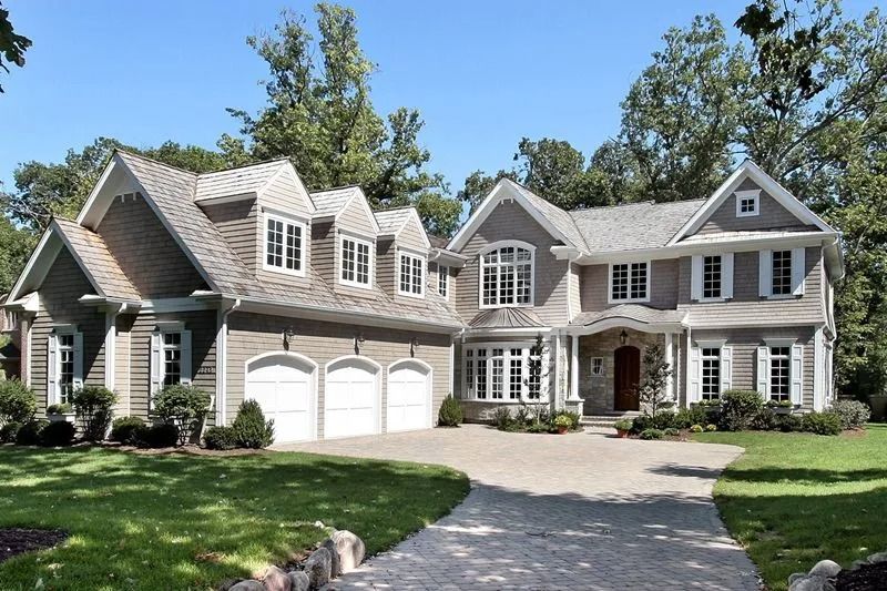Large, two-story gray house with a three-car garage, a curved driveway, and lush green lawn.