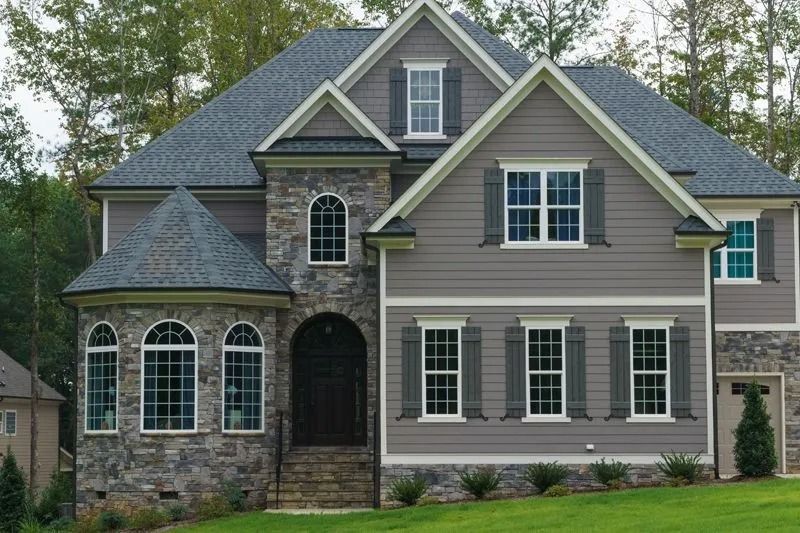 Two-story gray house with stone accents, gray roof, and green lawn.