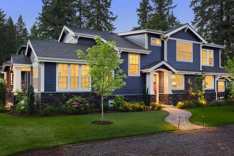 Blue house with white trim and a winding walkway. Green lawn and surrounding trees.
