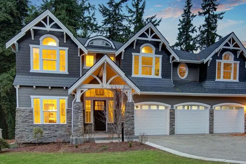 Two-story gray house with stone accents, white trim, arched windows, and three garage doors.