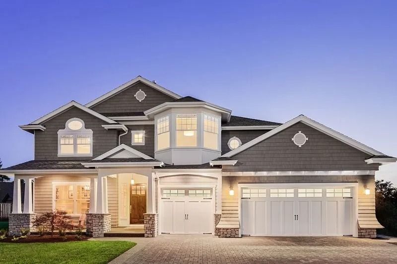 Two-story gray house with white trim, lit windows, two-car garage, and a lawn.