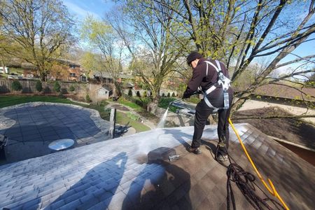 Man in safety harness pressure washing a roof on a sunny day.