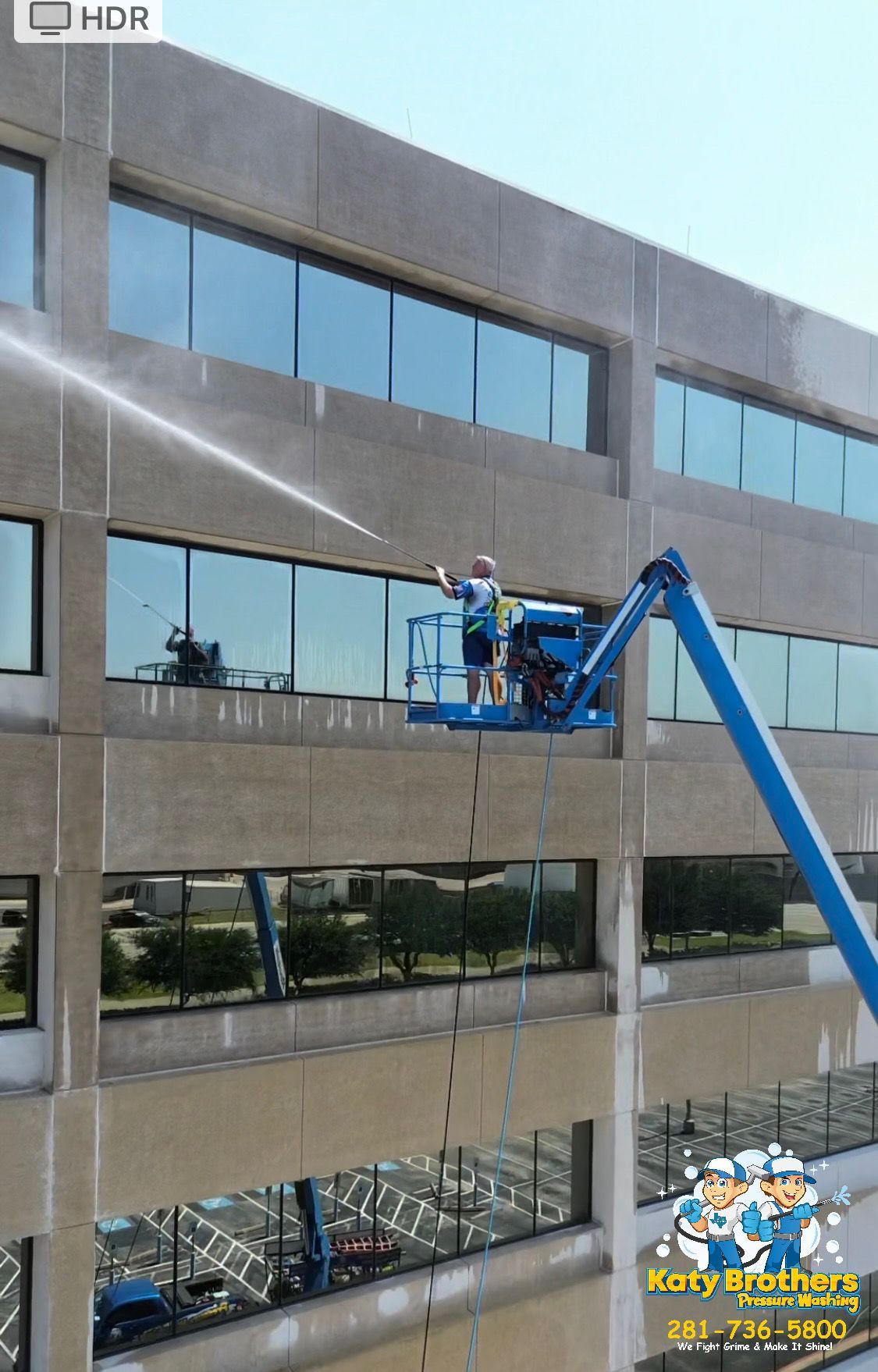 Worker on a blue boom lift cleaning windows on a multi-story office building.