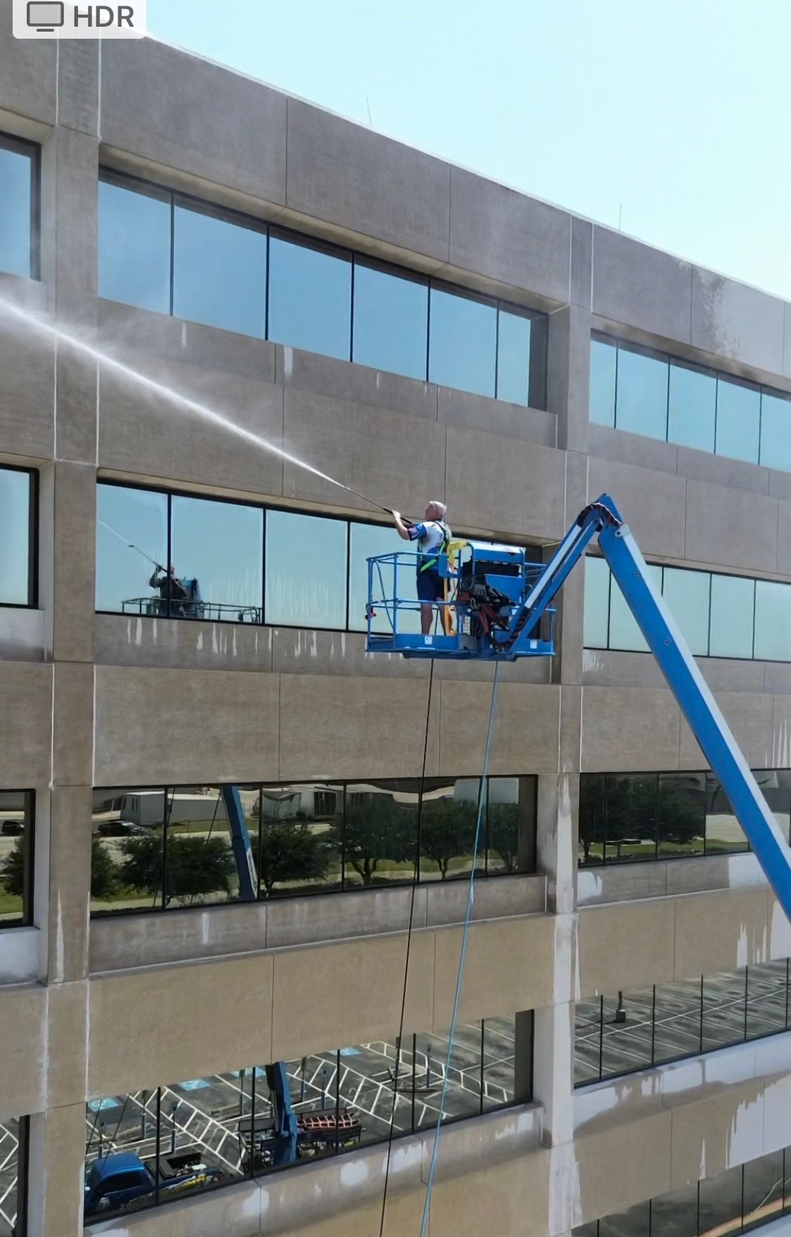 Man in lift washing windows on a multistory building; bright daylight