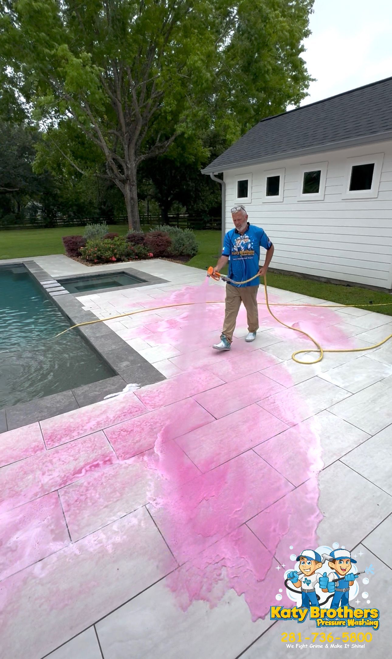 Person standing by a pool on a pink-painted patio near a white building and trees.