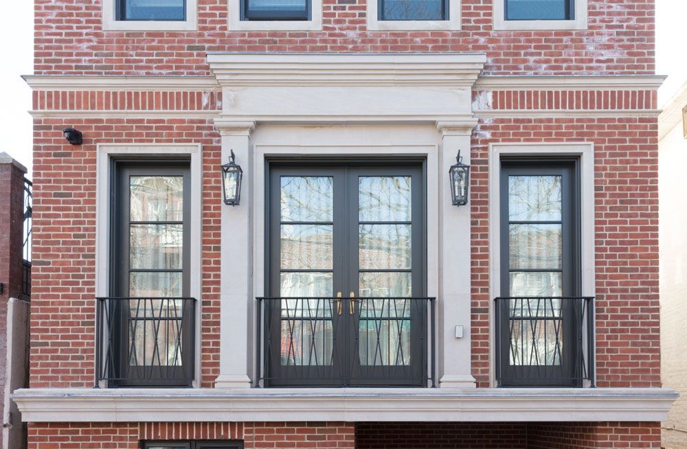 The front of a brick building with a balcony and black doors.