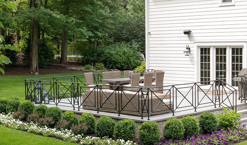 There is a patio with a table and chairs on it in front of a white house.