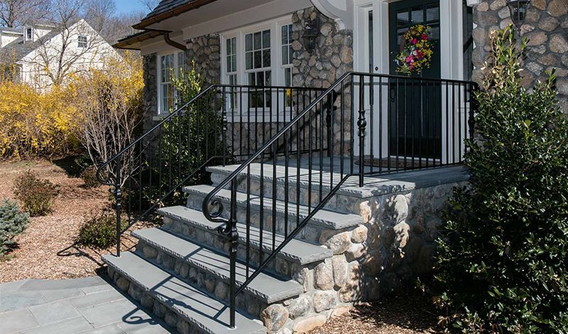 A stone house with stairs and a wrought iron railing.