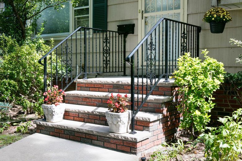 A front porch with brick steps and a wrought iron railing